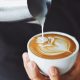 Close up of man pouring steamed milk into espresso creating a flower shape. Latte art, Coffee shops in La Jolla.