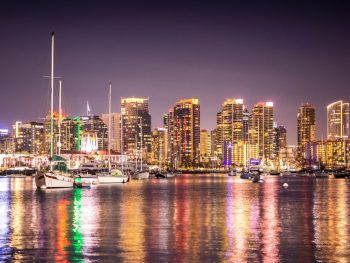 City skyline reflecting on water at night, boats sit on the colorful bay. San Diego skyline at night, Things to do in San Diego in November.