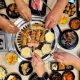overhead shot over Korean BBQ with hands reaching in and many side dishes on the table