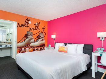 Hotel guest room with bright pink wall, and orange accent wall with large mural of roller skates. The Rambler Motel, Sesame Place San Diego Hotels.