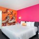 Hotel guest room with bright pink wall, and orange accent wall with large mural of roller skates. The Rambler Motel, Sesame Place San Diego Hotels.