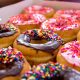 Close up photo of a box of donuts filled with chocolate and pink sprinkled donuts.