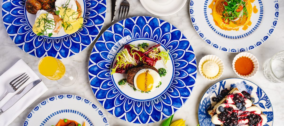 Decadent brunch spread on colorful blue plates with yellow tulips, coffee, and mimosas. San Diego Easter Brunch, Herb & Wood.