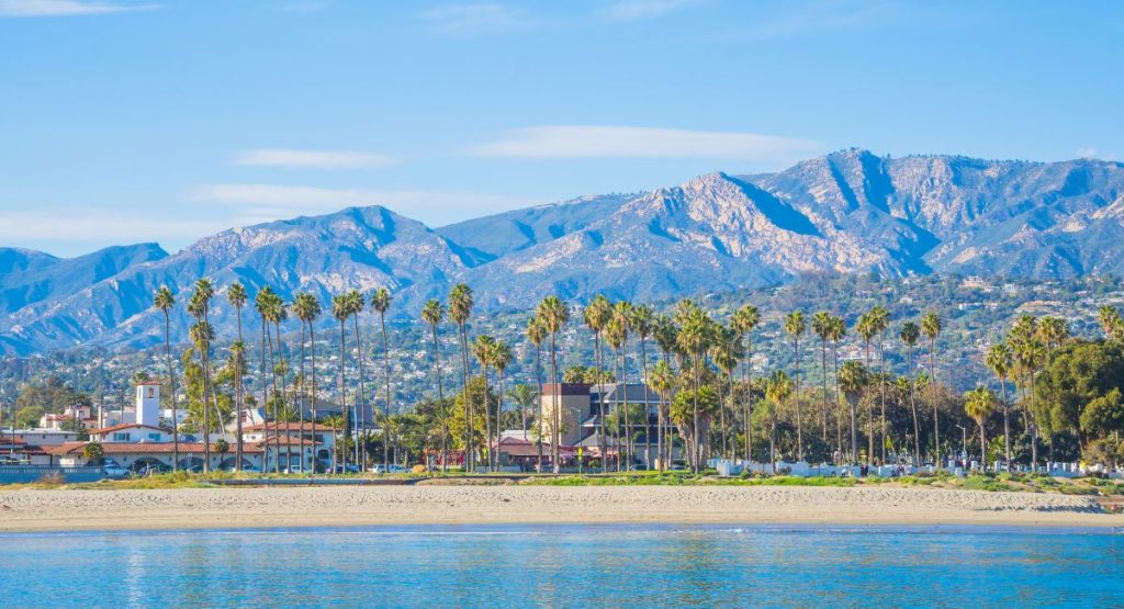 White sand beach lined with buildings and palm trees with large mountains in background. Santa Barbara, California.