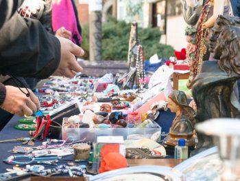 People looking at jewelry and goods on outdoor table at swap meet. Flea Market San Diego.